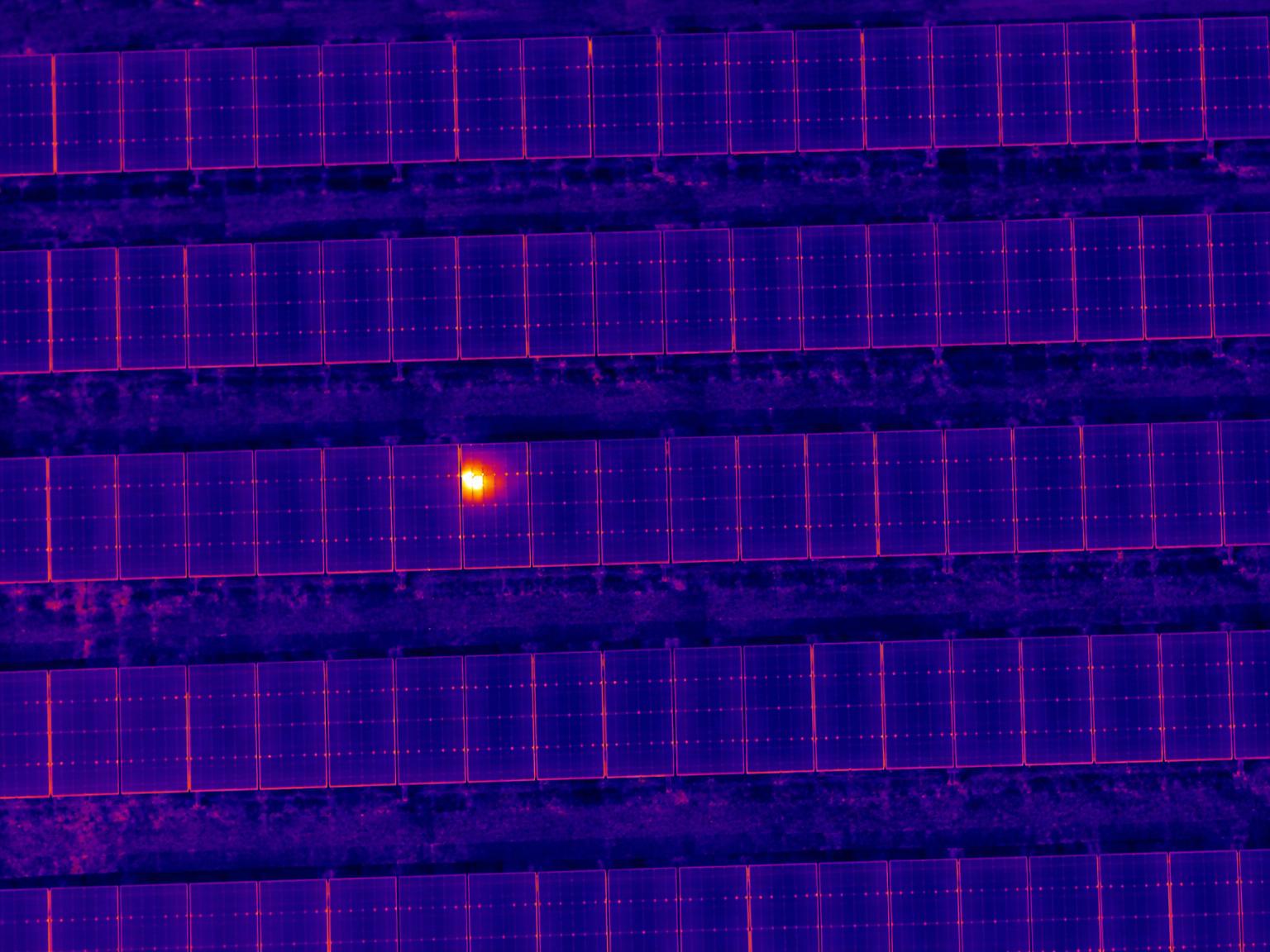 Thermal drone image of solar panel rows with one module glowing hot, outlined as a suspected hotspot